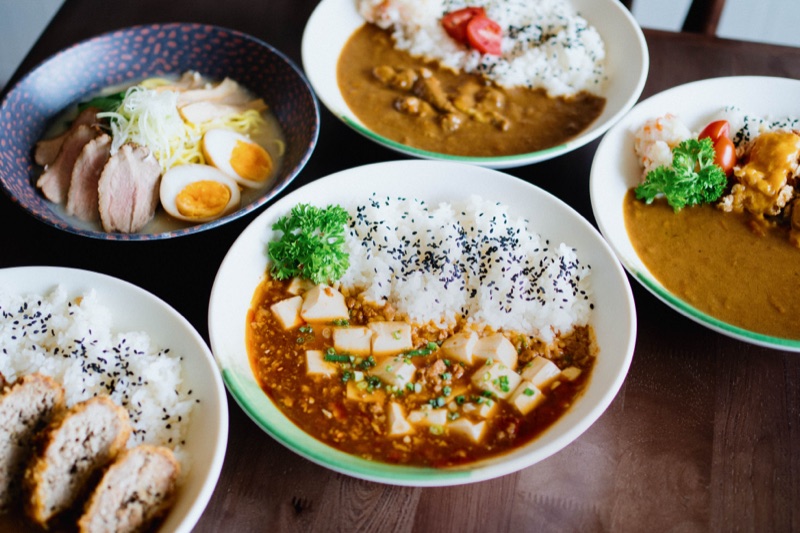 Mâm nhiều món Umidon: các phần cơm kare, cơm sốt Mala và tô ramen bày trên bàn gỗ